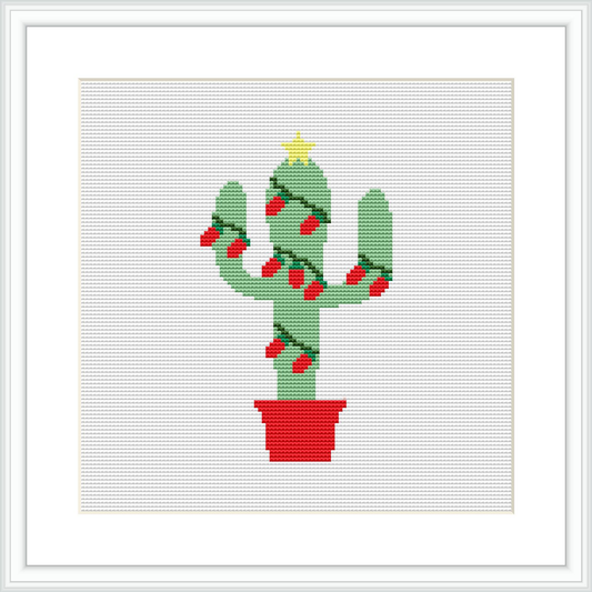 The image depicts a cross stitch pattern of a green cactus with multiple arms, decorated with red ornaments, and a yellow star on top. The cactus is placed in a red pot. The background is white, and the pattern appears to be framed.