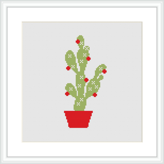 The image features a cross stitch pattern of a green cactus with multiple arms, each dotted with red Christmas ornaments. The cactus sits in a bright red pot and is displayed against a plain white fabric background within a simple, white square frame.