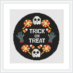 The image shows a circular cross-stitch pattern with a black background, featuring a white skull and crossbones, two green zombie hands, and three orange candies with white wrappers. A purple border surrounds the design, which is set within a square frame.