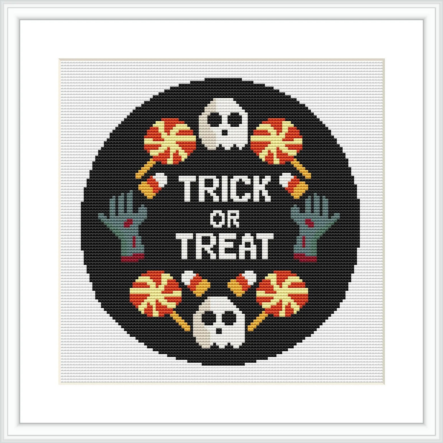 The image shows a circular cross-stitch pattern with a black background, featuring a white skull and crossbones, two green zombie hands, and three orange candies with white wrappers. A purple border surrounds the design, which is set within a square frame.