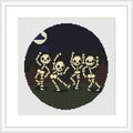 The image depicts a cross stitch pattern featuring three cartoon-like skeletons dancing in a group, placed within a dark circular backdrop resembling a full moon against a navy blue night sky. A small white crescent moon is at the top right corner.