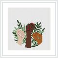 The image depicts a cross stitch pattern showcasing an arrangement of various leaf shapes in different shades of green. A stylized branch in brown extends through the design with a red and a beige decorative heart, each with small accent details.
