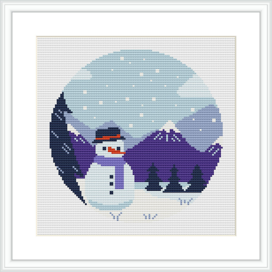 A framed cross stitch pattern depicting a circular winter landscape scene with a snowman in the center, surrounded by a mountain background, pine trees, and falling snowflakes, within a geometric patterned border.