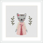 The image displays a cross stitch pattern design of a grey and white cat wearing a pink dress with a white apron. The cat is flanked by two olive green branches with leaves, set against a plain white background.