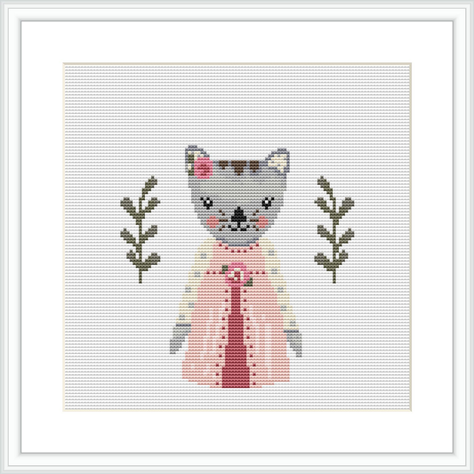 The image displays a cross stitch pattern design of a grey and white cat wearing a pink dress with a white apron. The cat is flanked by two olive green branches with leaves, set against a plain white background.