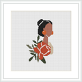 A framed cross stitch pattern depicting a side profile of a woman with her hair elegantly tied up, embellished with large, peach-pink floral accents and green foliage, against a plain white background.