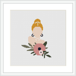 A framed cross stitch pattern depicts a stylized woman with a bun hairdo holding a large pink flower to her face, set against an off-white background.