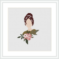 The image displays a framed cross stitch pattern depicting the upper torso of a stylized woman adorned with a floral arrangement. The pattern has a white background and is mounted within a simple, elegant frame.