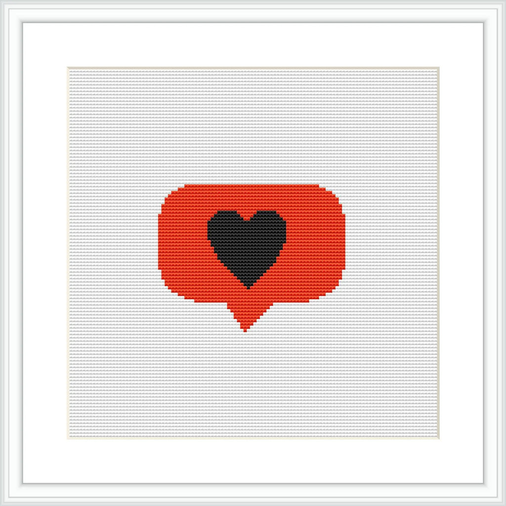 The image presents a cross stitch pattern framed in a white border. The pattern depicts a red speech bubble with a gray border containing a black heart in the center. The stitching is done on a white fabric which makes the colors stand out.