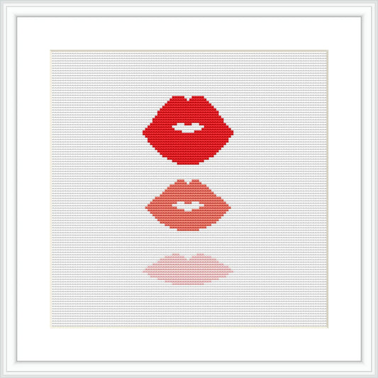 The image shows a cross stitch pattern of three sets of lips vertically aligned, each in a different shade ranging from deep red at the top to light pink at the bottom, against a plain white background. It is situated within a simple white frame.