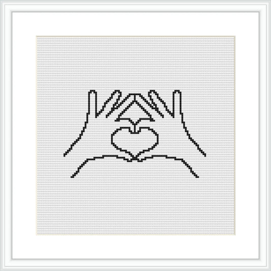 The image shows a framed cross stitch pattern depicting two hands forming a heart shape in the center. The stitches are made in a single color on a plain white canvas.