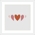 The image shows a cross stitch pattern with three heart shapes in a row, each decreasing in size from left to right. The hearts are filled with different shades of terra cotta and pink, creating a gradient effect. The pattern is displayed within a simulated white frame against a white background.