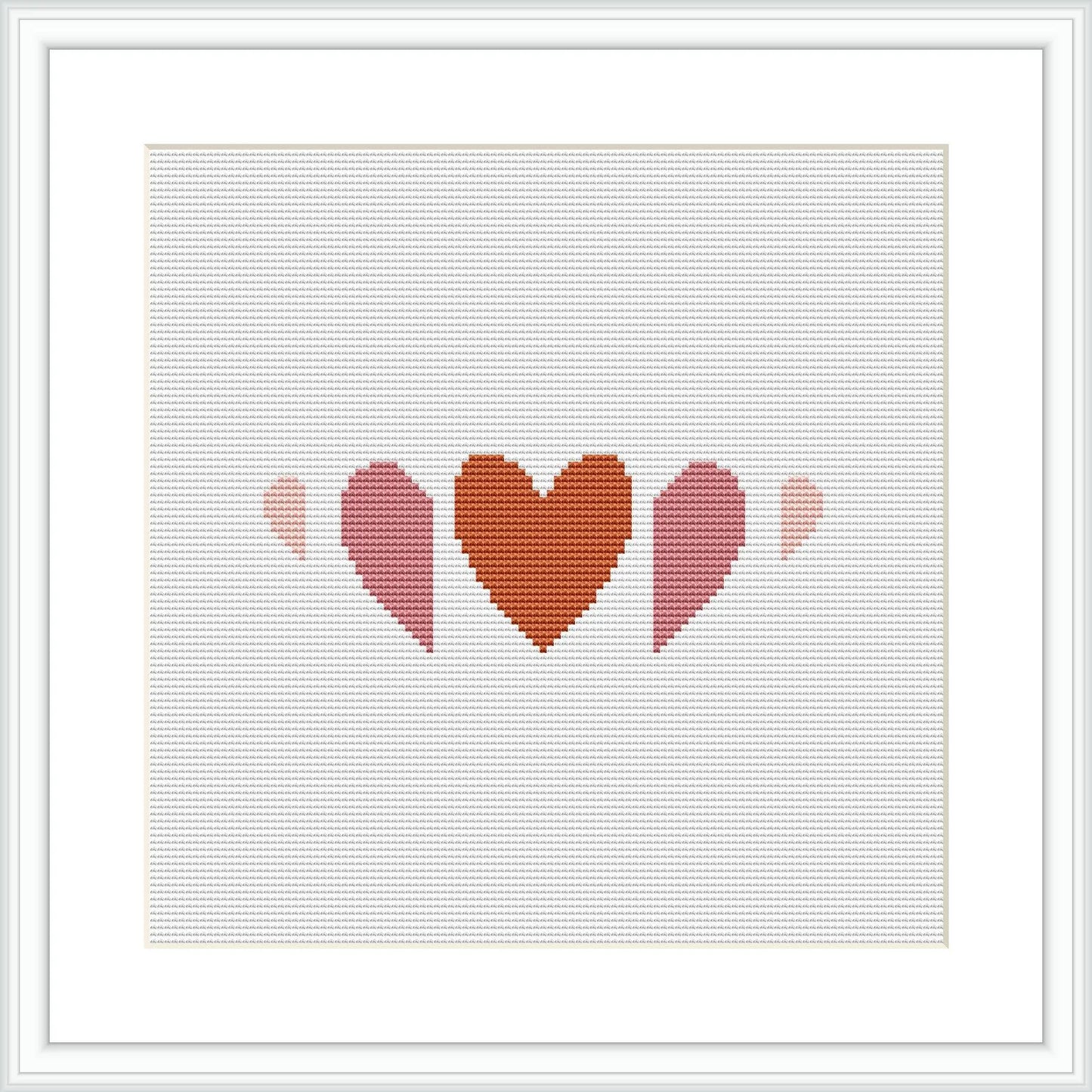 The image shows a cross stitch pattern with three heart shapes in a row, each decreasing in size from left to right. The hearts are filled with different shades of terra cotta and pink, creating a gradient effect. The pattern is displayed within a simulated white frame against a white background.