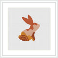 The cross stitch pattern depicts a stylized rabbit in profile with sections of various warm hues, framed within a white border on a square canvas.