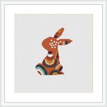 The image shows a stylized bunny in profile, stitched during Easter with a pattern predominantly featuring purple, orange, olive green, brown, and cyan colors. The bunny is enclosed in a square frame, signifying that it is a pattern design ready for cross stitching.