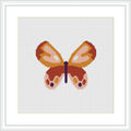The image shows a framed cross stitch pattern of a stylized butterfly centered on a white canvas, with a color palette consisting of pastel pinks, oranges, yellows, and browns.