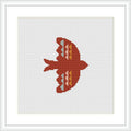 The image displays a cross stitch pattern of a bird silhouette in red, coral, and peach tones against a white background, framed in a simple white frame, suggesting a minimalist and symmetrical design.