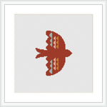 The image displays a cross stitch pattern of a bird silhouette in red, coral, and peach tones against a white background, framed in a simple white frame, suggesting a minimalist and symmetrical design.