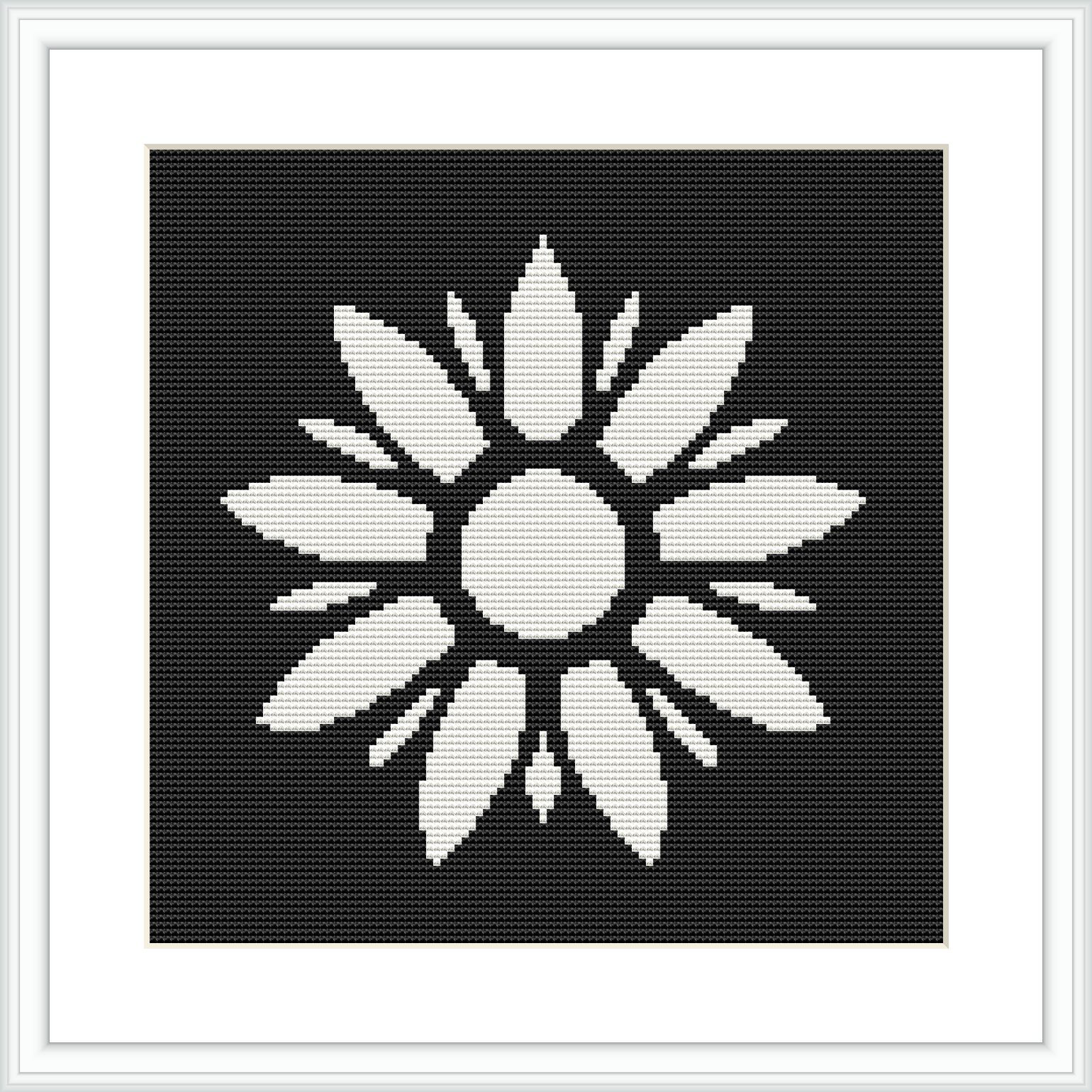 The image depicts a black and white cross stitch pattern of a symmetrical floral design with a central circle surrounded by elongated petal-like shapes. It is placed within a square frame against a black background.