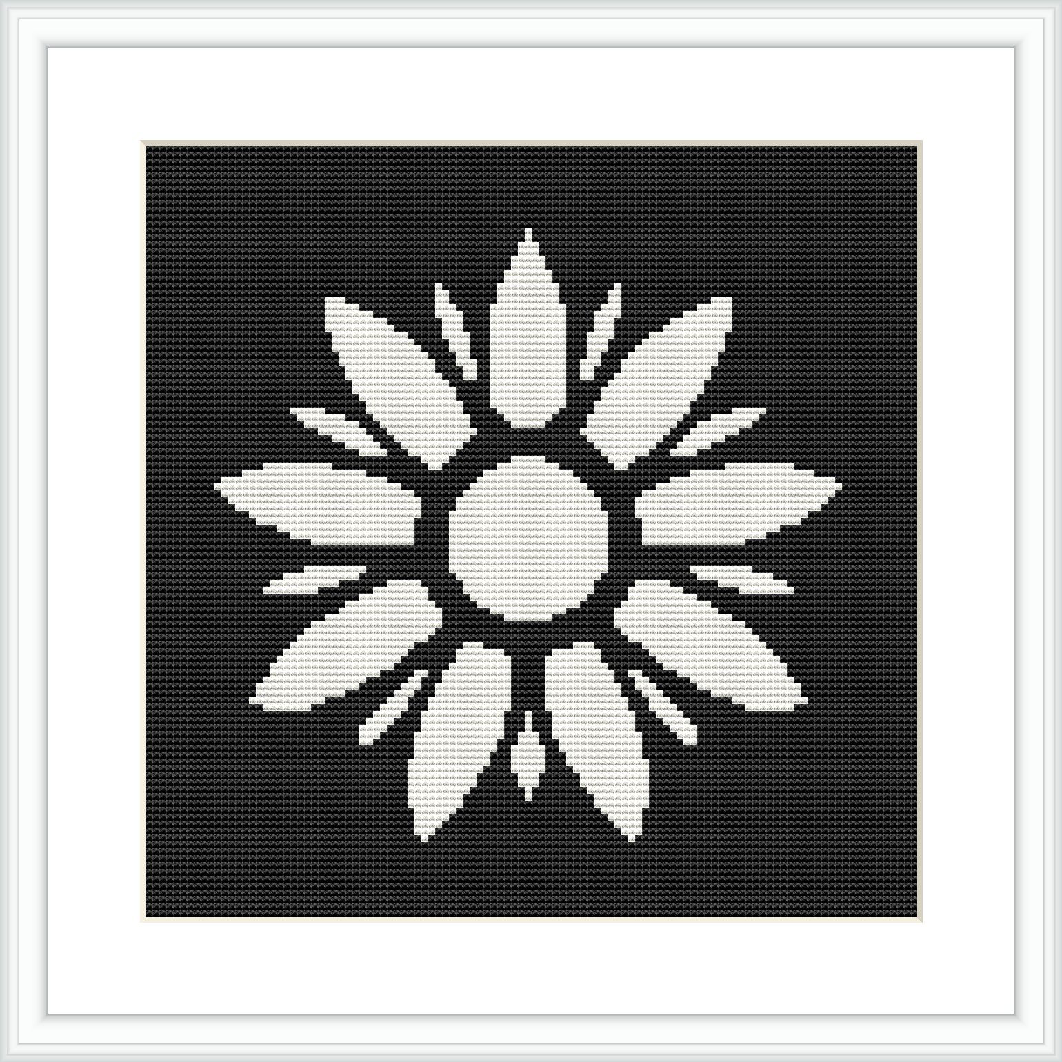 The image depicts a black and white cross stitch pattern of a symmetrical floral design with a central circle surrounded by elongated petal-like shapes. It is placed within a square frame against a black background.