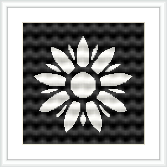 The image depicts a black and white cross stitch pattern of a symmetrical floral design with a central circle surrounded by elongated petal-like shapes. It is placed within a square frame against a black background.