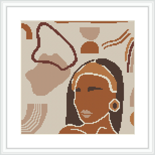 The image showcases a cross-stitch pattern framed in white, depicting a stylized woman with a headscarf and earring. The background includes abstract shapes resembling desert elements.