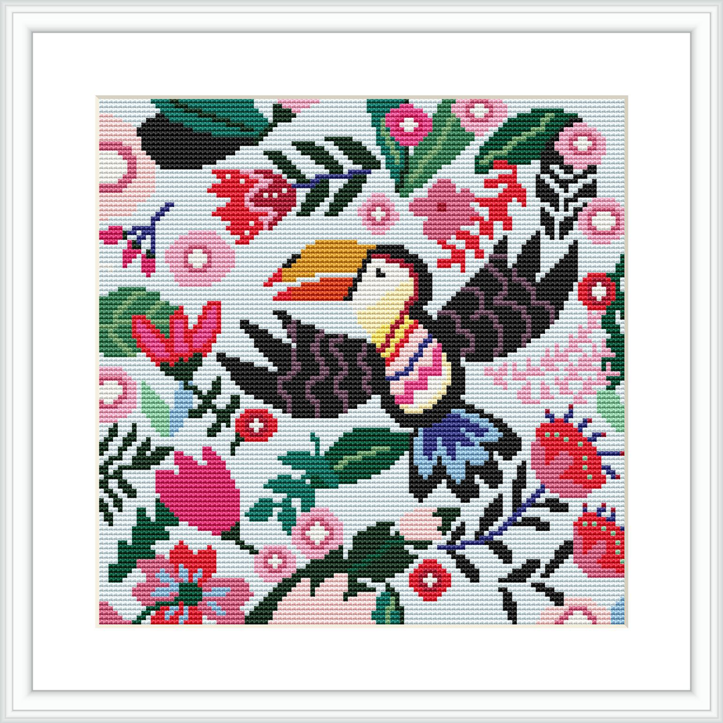 A cross stitch pattern of a colorful toucan surrounded by a lush variety of flowers and leaves. The embroidery is framed and showcases detailed stitching on a white grid-based background.