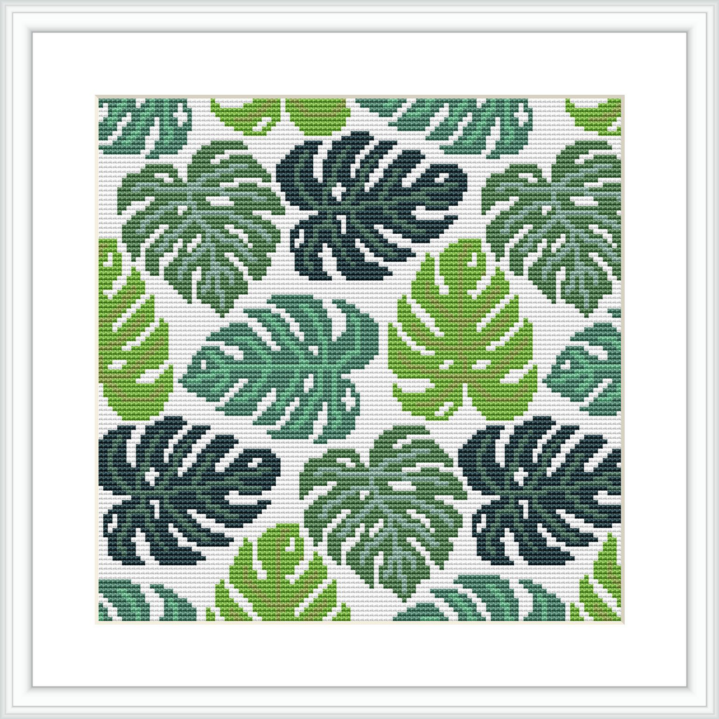 The image shows a cross stitch pattern depicting stylized monstera leaves in various shades of green, arrayed in a repetitive, tessellated design on a white background, framed in white.