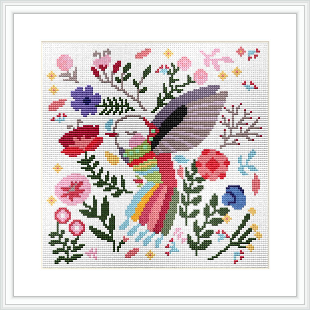 The scene depicts a colorful hummingbird in the center, surrounded by various types of flowers and leaves in multiple hues, stitched against a white background, all within a square frame.