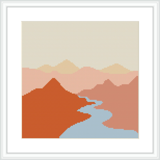 The cross stitch pattern depicts a stylized river landscape with geometric shapes representing mountains in shades of pink and red, with a river in light blue, set against a pale background suggesting the sky.