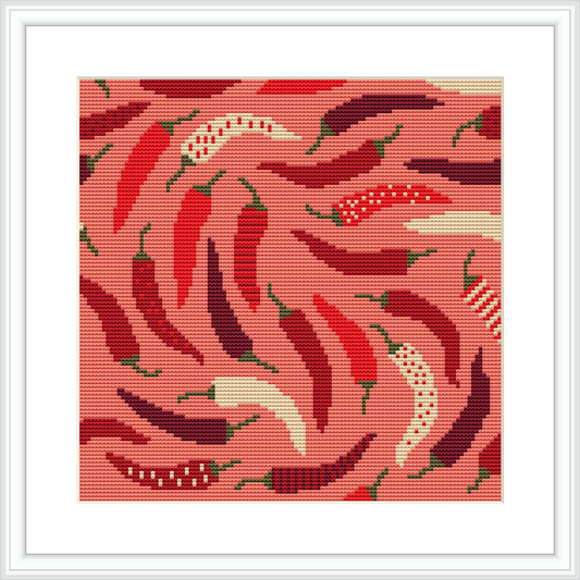 The image displays a cross stitch pattern featuring red chili peppers with green stems, interwoven in a swirling, spiral motion against a dotted pink and maroon background. It's framed with a white border within a simulated picture frame.