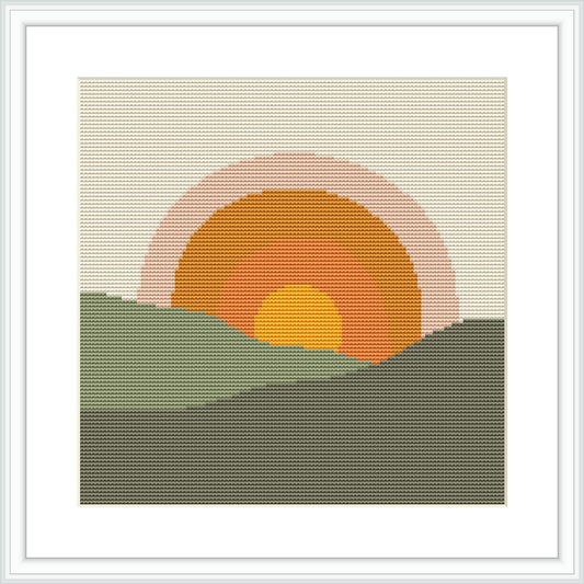 The image depicts a cross stitch pattern showcasing a setting sun with a gradient of orange and pink hues above a silhouette of dark green hills.