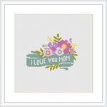 The image depicts a cross stitch design featuring a floral arrangement with the text 'I Love You Mom'. The flowers are in hues of purple, pink, and yellow, with green foliage, all framed within a white canvas.