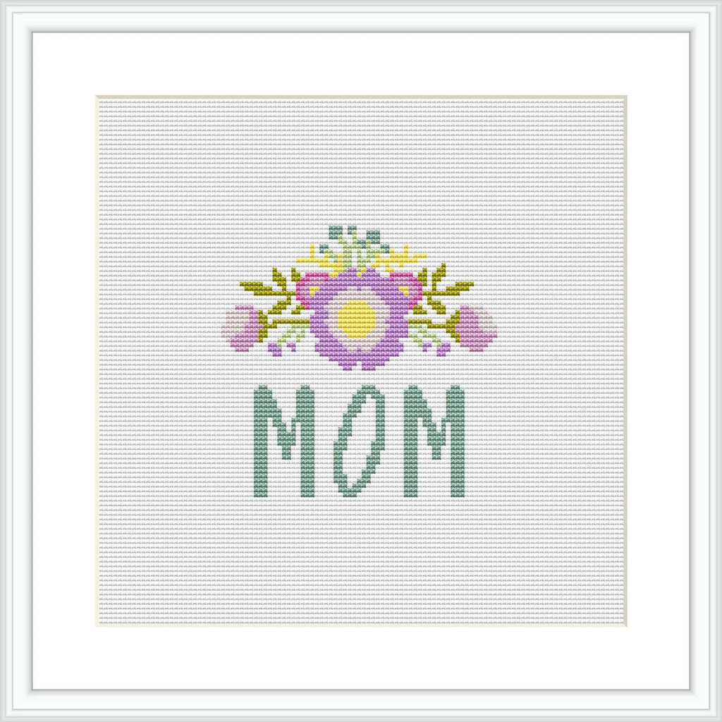 The image contains a cross stitch pattern featuring the word 'MOM' in green letters at the bottom, with a decorative floral arrangement above it showcasing a bouquet with purple and yellow accents on a white background.