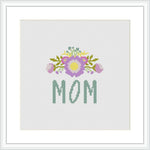 The image contains a cross stitch pattern featuring the word 'MOM' in green letters at the bottom, with a decorative floral arrangement above it showcasing a bouquet with purple and yellow accents on a white background.