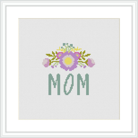 The image contains a cross stitch pattern featuring the word 'MOM' in green letters at the bottom, with a decorative floral arrangement above it showcasing a bouquet with purple and yellow accents on a white background.