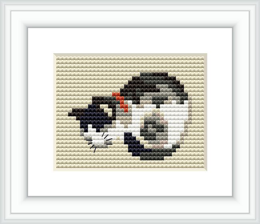 The image depicts a small cross stitch pattern of a sleeping cat curled up. The cat is primarily gray with black stripes, white markings, and a small patch of red. The background of the pattern is beige, and the design is framed in a simple white border.