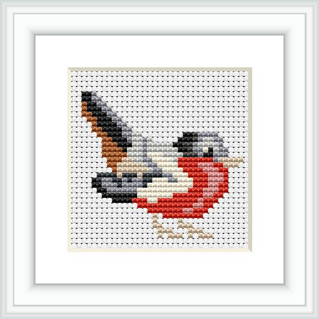 The image shows a framed cross stitch pattern of a bird. The bird has a predominantly beige body with a red breast, black accents, and grey wings. It is centered on a white cross-stitch canvas within a simple white frame.