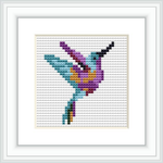 The image features a framed cross stitch pattern depicting a stylized hummingbird in mid-flight. The embroidery is done on aida cloth, showcased within a white square frame set against a white background.