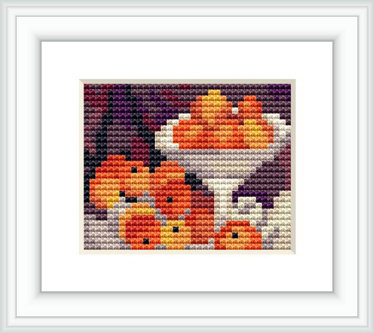 The image showcases a cross stitch pattern depicting a still life arrangement of apples and oranges in a bowl against a dark background.