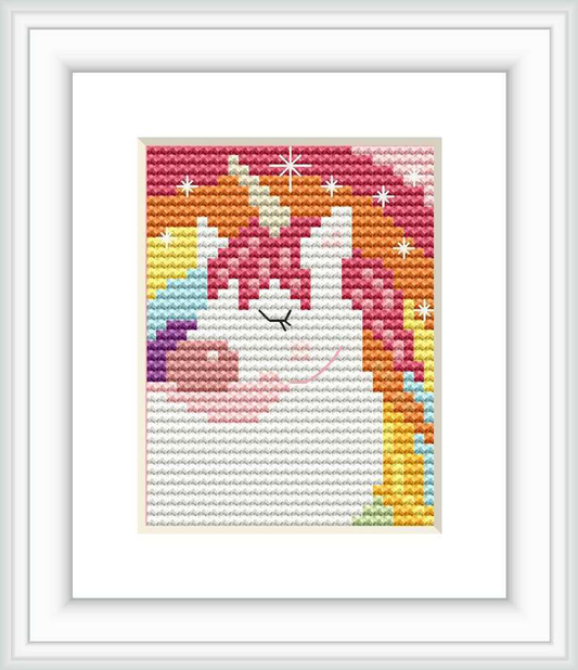 The image displays a framed cross stitch pattern of a stylized unicorn with a rainbow mane and stars around it. It is executed in bright and pastel colors against a plain background within a white frame.