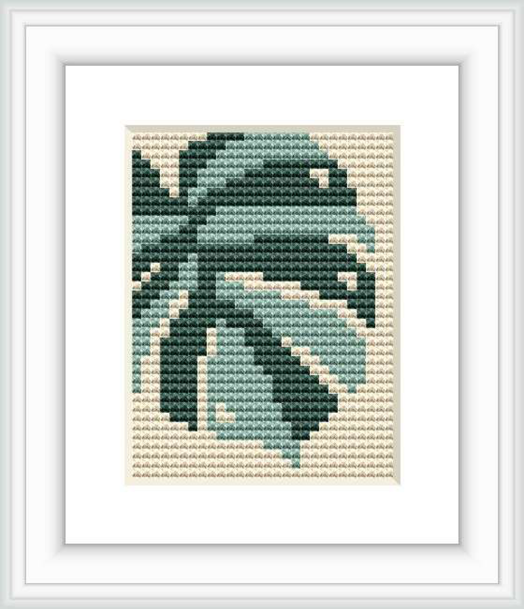 The image shows a framed cross stitch pattern with a zoomed-in monstera leaf design. The pattern is predominantly green with different shades for depth, stitched on a beige cross stitch cloth and surrounded by a white border inside a simple frame.