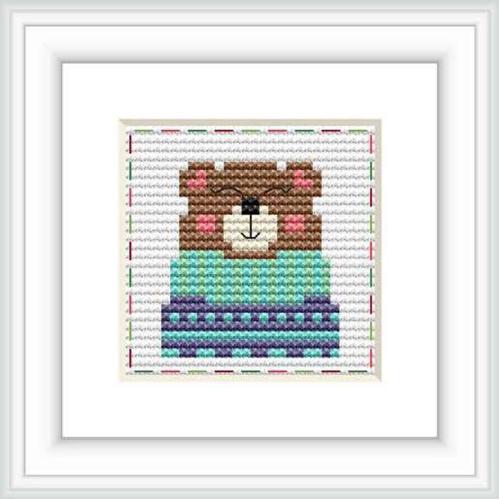 The image displays a framed cross stitch pattern of a stylized bear centered on a grid-based cloth with a combination of colored stitches.