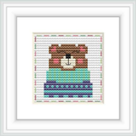 The image displays a framed cross stitch pattern of a stylized bear centered on a grid-based cloth with a combination of colored stitches.