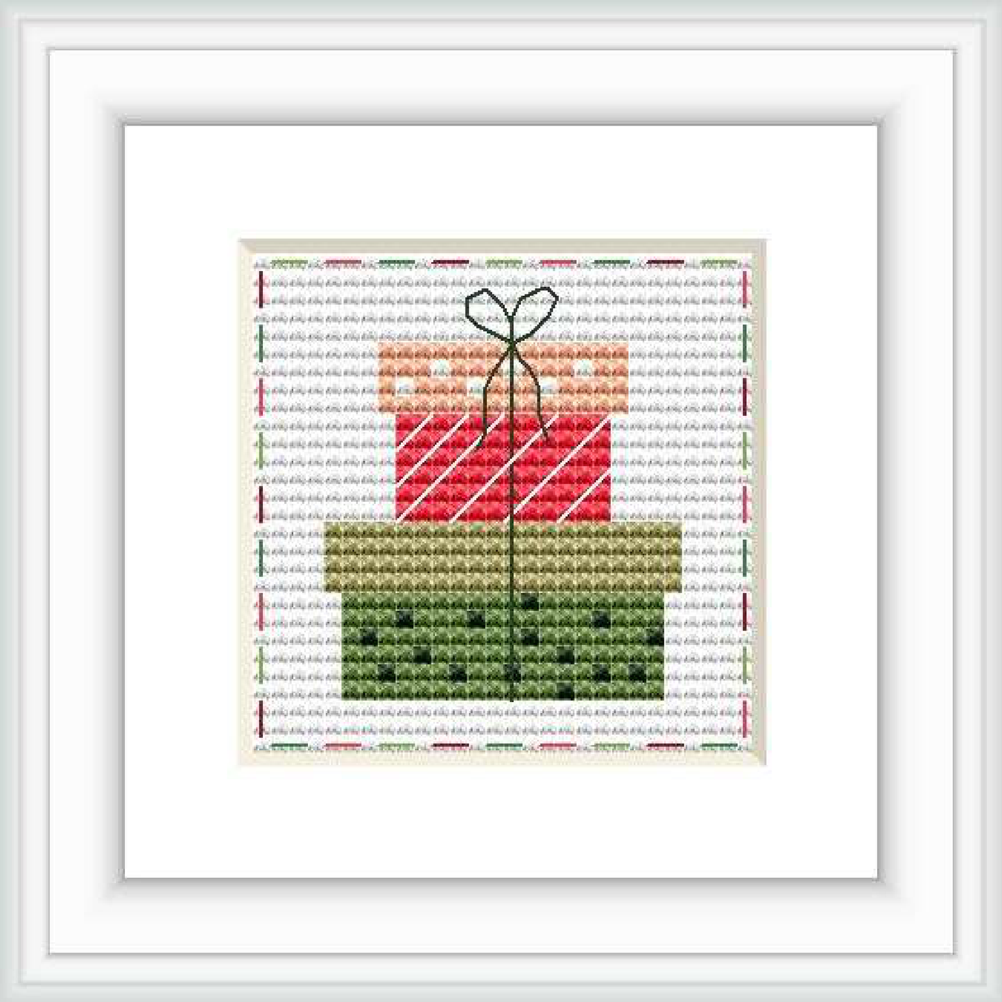 The image shows a cross stitch pattern framed in white, depicting a stylized gift box with a bow on top. The pattern is set against a patterned background with faint script text. The gift box has diagonal red and white stripes, and the bow appears to be a darker shade of green.