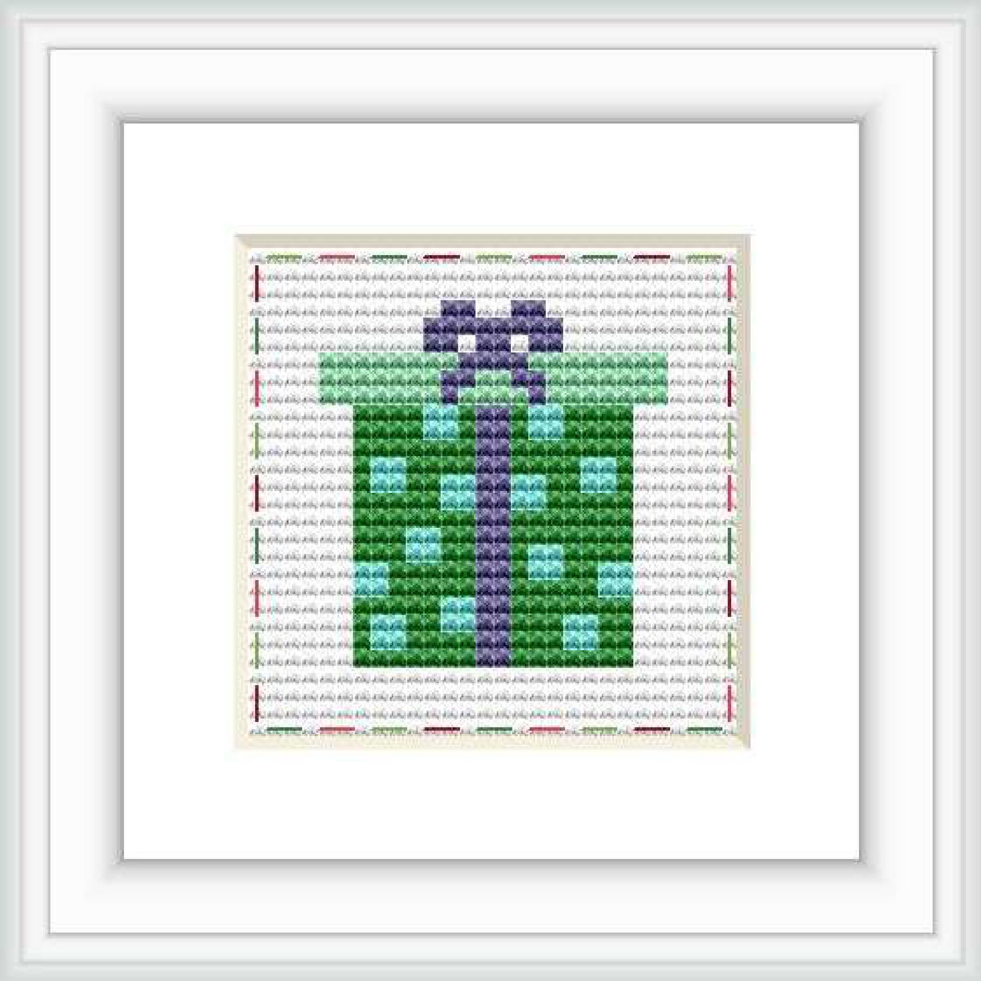 This is a framed cross stitch image depicting a stylized wrapped gift with a bow, primarily in green and purple hues. It's set on a white background with red and grey decorative stitches around the border.