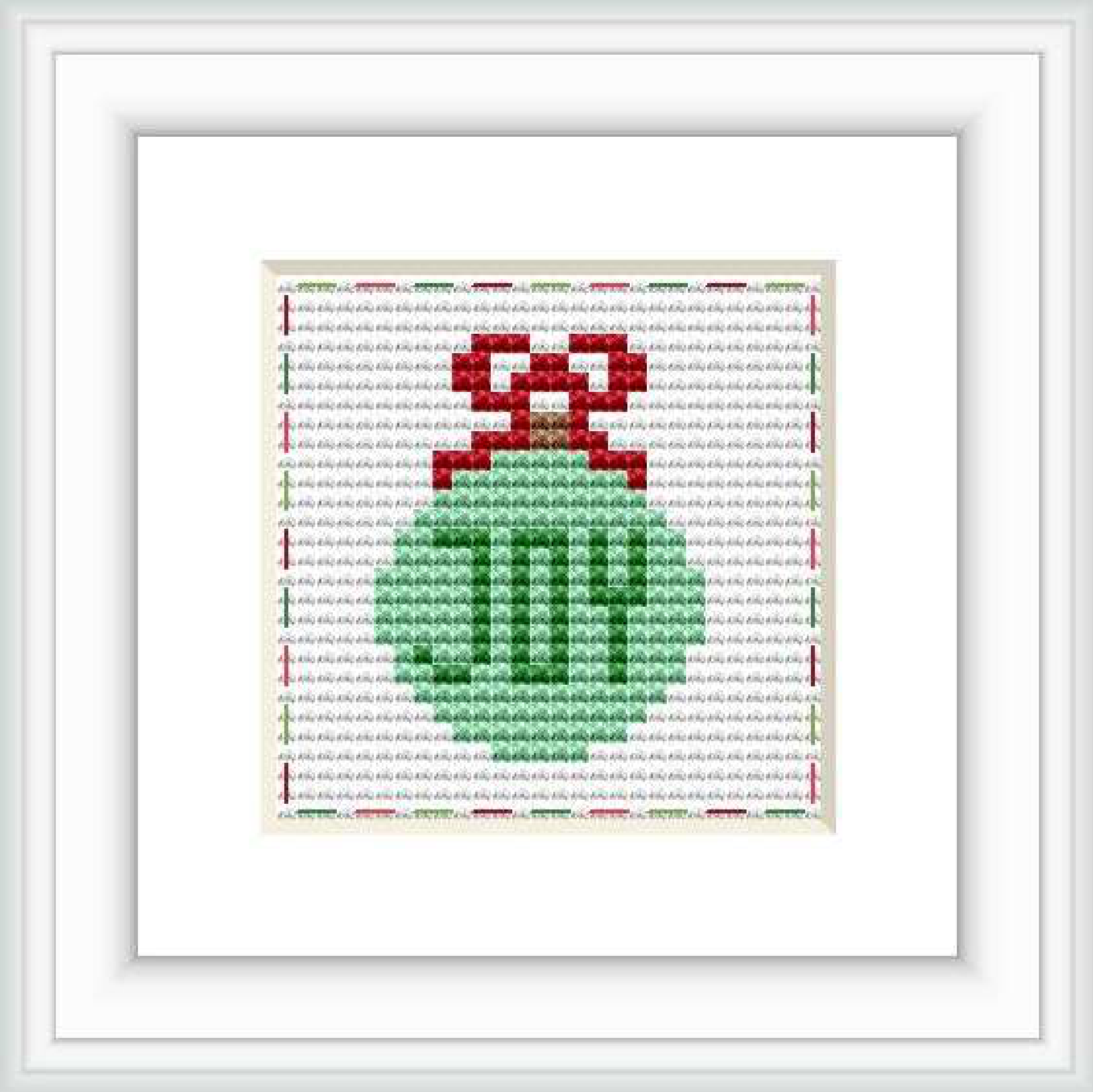 The image features a framed cross stitch of a green Christmas ornament with a red ribbon on a patterned light grey background. The cross stitch is centralized within a white mat and a simple black frame.
