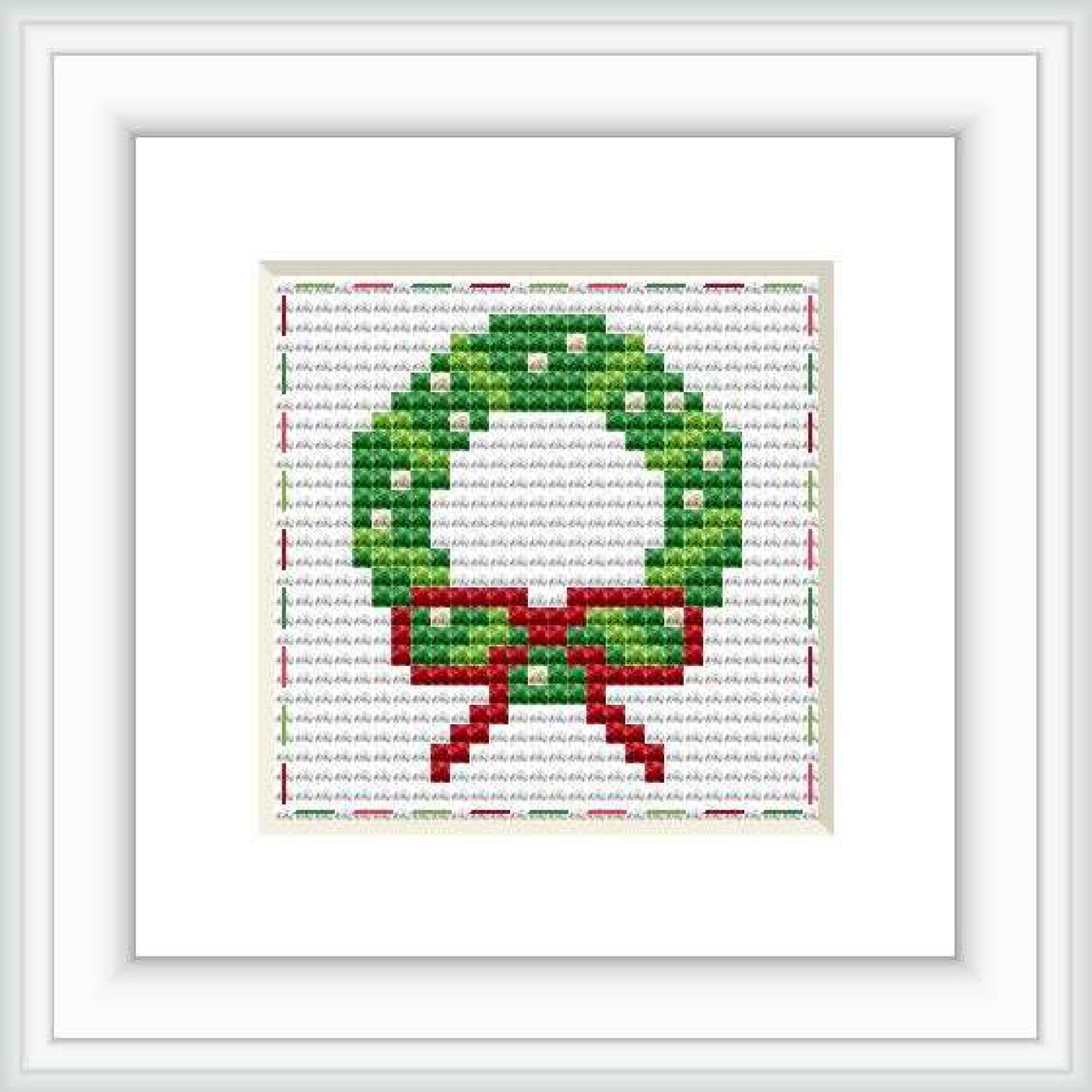 The image shows a framed cross stitch pattern of a holiday wreath with a red bow, against a white background. The stitches are visible and display a 28 by 28 grid pattern.