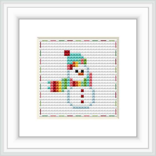 The image shows a framed cross stitch pattern of a stylized snowman against a patterned background within a square frame. The snowman is made with colorful blocks that form a rainbow gradient.