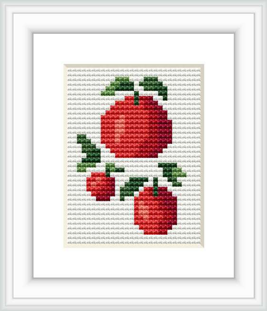 The image shows a framed cross stitch pattern featuring several red apples with green leaves on a plain white background, stitched on a linen or aida fabric.